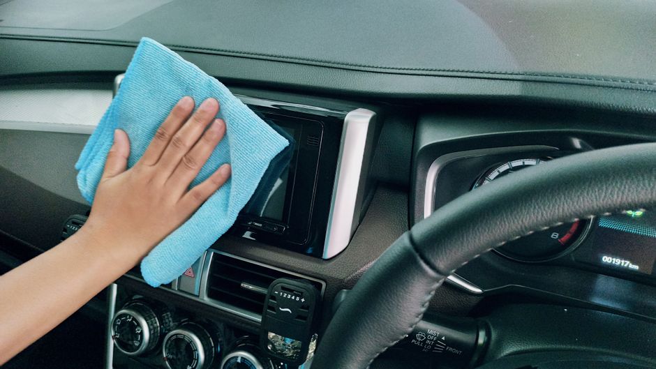 Crop anonymous person polishing panel in right hand drive car by using blue fiber cloth